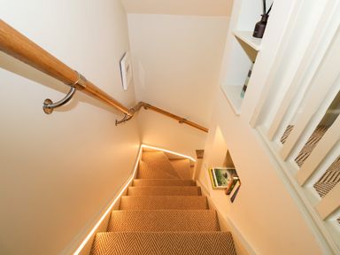A carpeted staircase with wooden handrails and built-in shelves on the wall at The Cabin at Ropewalk in Goonbell near St Agnes