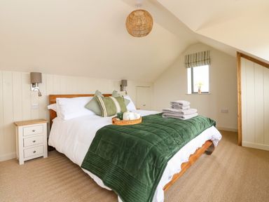 A bedroom with a double bed with green pillows and blanket bedside tables and a small window at The Cabin at Ropewalk Goonbell near St Agnes