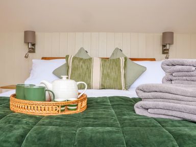 A bed with green and white pillows a green quilt a tray with a white teapot green mugs and a stack of folded towels at The Cabin at Ropewalk in Goonbell near St Agnes