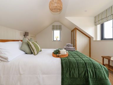 A bedroom with a bed green and white bedding and folded towels by windows at The Cabin at Ropewalk in Goonbell near St Agnes