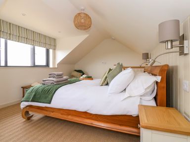 A bedroom with a wooden bed with white and green bedding and folded towels on the bed at The Cabin at Ropewalk Goonbell near St Agnes