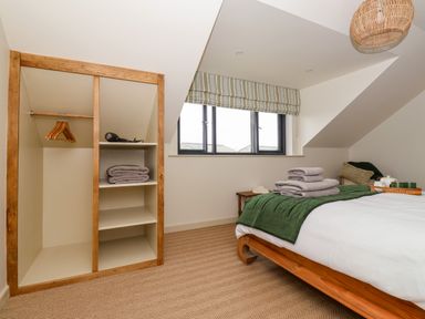 A bedroom with a wooden bed and folded towels near a window with striped blinds at The Cabin at Ropewalk in Goonbell near St Agnes