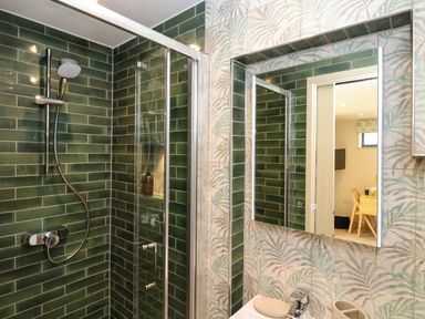 A bathroom with a green tiled shower, glass shower door, and a mirror above a sink at The Cabin at Ropewalk in Goonbell near St Agnes
