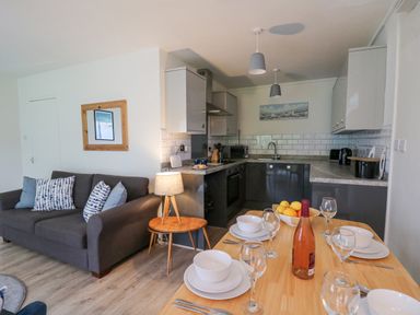 A kitchen and dining area with a gray couch and table set for four at 14 Coedrath Park in Saundersfoot