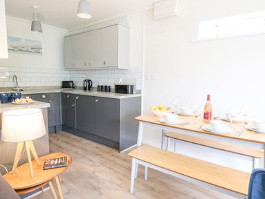 A kitchen with gray cabinets and a wooden dining table with benches set with dishes and a bottle at 14 Coedrath Park Saundersfoot