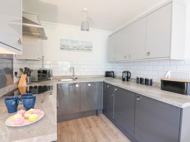 A kitchen with grey cabinets white subway tile backsplash countertop with kettle toaster microwave and a plate of cupcakes at 14 Coedrath Park Saundersfoot