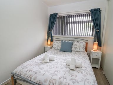 A bedroom with a double bed with elephant patterned bedding two bedside tables with lamps and blue curtains at 14 Coedrath Park in Saundersfoot