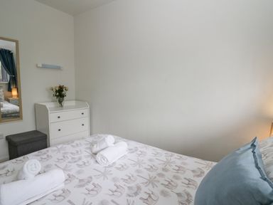 A bedroom with a bed with patterned bedding and rolled towels a white chest of drawers with flowers and a mirror at 14 Coedrath Park Saundersfoot