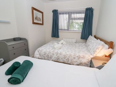 A bedroom with two beds a window with blue curtains a chest of drawers and towels on one bed at 14 Coedrath Park in Saundersfoot