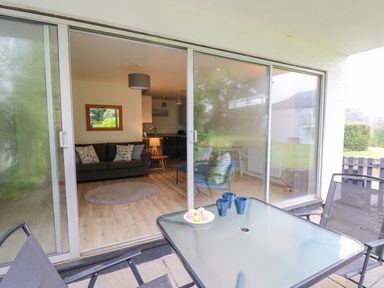A patio with table and chairs looking into a living room with sofa and round rug at 14 Coedrath Park in Saundersfoot