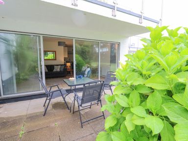 A patio with glass table and four chairs outside sliding glass doors showing a living room with sofa and lamp 14 Coedrath Park Saundersfoot