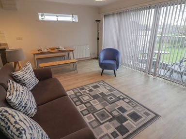 A living area with a brown sofa with patterned cushions a blue armchair a wooden dining table with benches and a floor lamp at 19 Coedrath Park in Saundersfoot