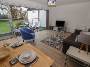A living room with a sofa a blue chair a dining table set near sliding glass doors leading to a balcony at 19 Coedrath Park in Saundersfoot