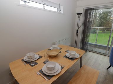 A dining table set for four with white dishes and glasses in a room with a floor lamp and sliding glass door at 19 Coedrath Park in Saundersfoot