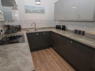 A kitchen with grey countertops black lower cabinets light grey upper cabinets a sink stove toaster kettle and canisters at 19 Coedrath Park in Saundersfoot