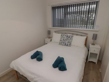 A bedroom with a double bed white bedding and two rolled blue towels by the window at 19 Coedrath Park Saundersfoot