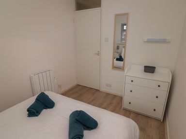 A bedroom with a bed and rolled towels on it a white dresser with a basket and a wall mirror above at 19 Coedrath Park in Saundersfoot