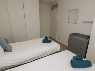 A bedroom with two single beds with white bedding blue pillows and rolled towels a grey chest of drawers and a mirror on the wall at 19 Coedrath Park in Saundersfoot