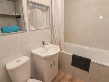 A bathroom with a toilet sink cabinet round mirror bathtub and towels at 19 Coedrath Park Saundersfoot