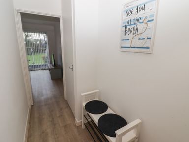 A hallway with a white bench and two black seat cushions and a sign on the wall that reads see you at the beach at 19 Coedrath Park in Saundersfoot