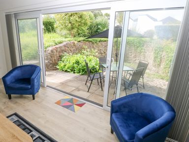A room with two blue armchairs facing glass sliding doors leading to a patio with a table and chairs at 29 Coedrath Park in Saundersfoot