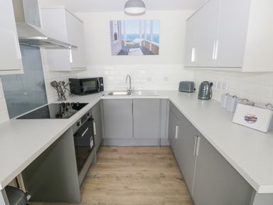 A kitchen with grey cabinets a black microwave a kettle and toaster on the counter and a painting above the sink at 29 Coedrath Park Saundersfoot