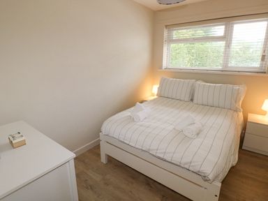 A bedroom with a bed striped bedding rolled towels two bedside tables with lamps and a window at 29 Coedrath Park Saundersfoot