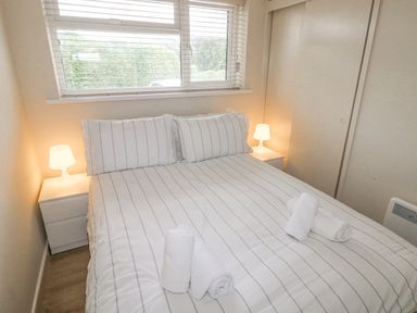 A bedroom with a double bed striped bedding two bedside tables with lamps and rolled towels on the bed at 29 Coedrath Park in Saundersfoot
