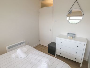 A bedroom with a bed, white dresser, round mirror, and a gray storage bench at 29 Coedrath Park in Saundersfoot