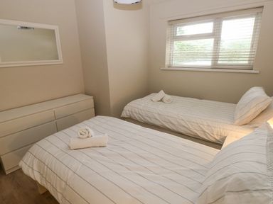 A bedroom with two single beds a white dresser and a window with blinds at 29 Coedrath Park in Saundersfoot