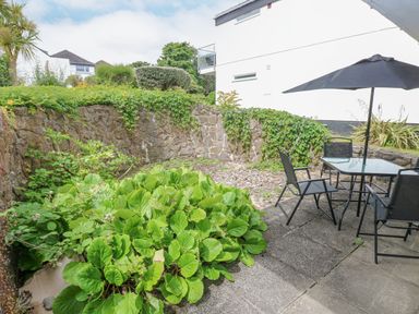 A garden patio with chairs and a table under an umbrella next to plants and a stone wall at 29 Coedrath Park in Saundersfoot