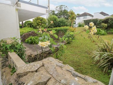 A garden with stone walls grass bushes and flowers near residential houses at 29 Coedrath Park in Saundersfoot