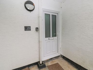 A white door with frosted glass panels on a textured white wall with a black light fixture and house number 29 Coedrath Park Saundersfoot