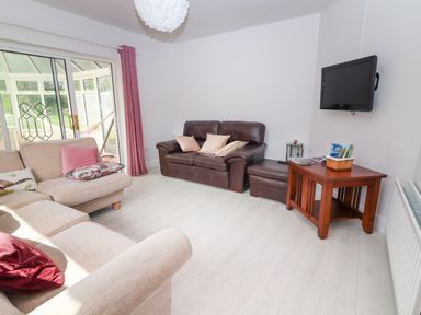 A living room with beige and brown sofas a wooden table and a wall-mounted TV at Tonakilla House in Tonakilly near Camp County Kerry