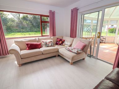 A beige corner sofa with cushions in front of large windows and sliding glass doors at Tonakilla House Tonakilly near Camp County Kerry