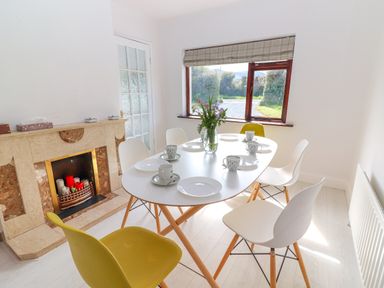 A dining area with a white table surrounded by white and yellow chairs set with plates cups and a vase of flowers by a window at Tonakilla House in Tonakilly near Camp County Kerry