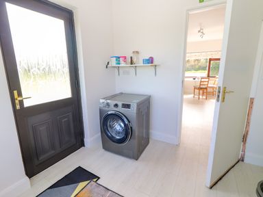 A laundry room with a washing machine near a door and a shelf with containers at Tonakilla House Tonakilly near Camp County Kerry