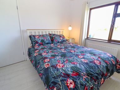 A bedroom with a bed with a floral patterned bedspread a bedside table with a lamp and a window at Tonakilla House Tonakilly near Camp County Kerry