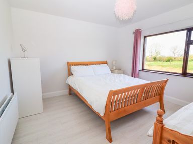 A bedroom with a wooden bed a white dresser a bedside table with a lamp and a large window with purple curtains at Tonakilla House in Tonakilly near Camp County Kerry