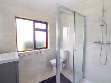 A bathroom with a shower, toilet, sink, window with frosted glass, and a dark floor mat at Tonakilla House in Tonakilly near Camp County Kerry