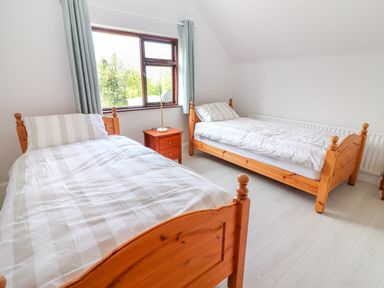 A bedroom with two wooden single beds a nightstand with a lamp and a window with curtains at Tonakilla House Tonakilly near Camp County Kerry