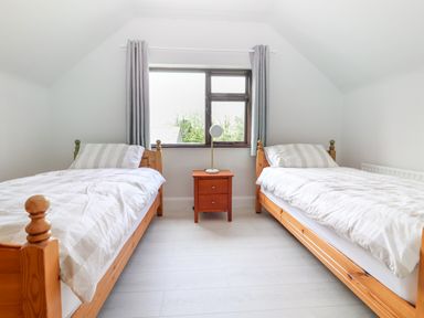 A bedroom with two single beds a wooden nightstand with a lamp and a window with gray curtains at Tonakilla House Tonakilly near Camp County Kerry