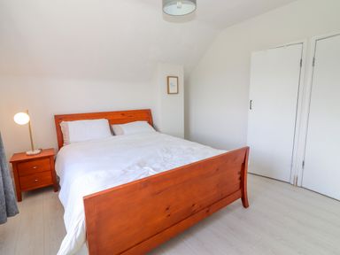 A bedroom with a wooden bed frame white bedding a wooden nightstand with a lamp and white doors at Tonakilla House Tonakilly near Camp County Kerry