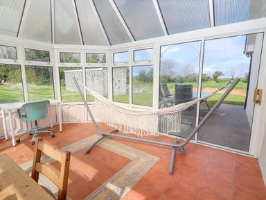 A conservatory with a hammock on a stand a turquoise office chair a white desk and a wooden chair at Tonakilla House Tonakilly near Camp County Kerry