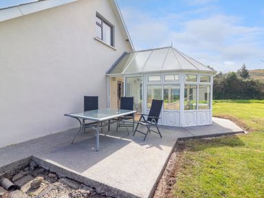 An outdoor patio area with a glass table and three black chairs next to a white conservatory at Tonakilla House Tonakilly near Camp County Kerry