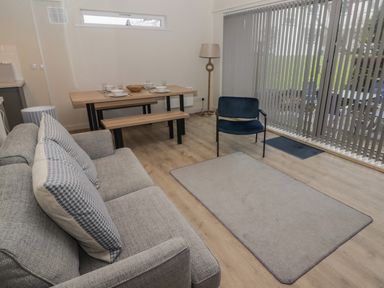A living room with a gray sofa, blue armchair, wooden dining table with benches, floor lamp, and vertical blinds at 23 Coedrath Park Saundersfoot