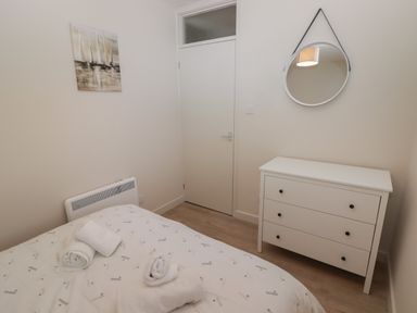 A bedroom with a bed covered with a patterned duvet and rolled towels a white chest of drawers and a round mirror at 23 Coedrath Park in Saundersfoot