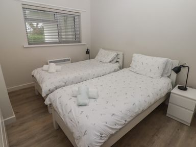 A bedroom with two single beds with white bedding a nightstand with a black lamp and a window with blinds at 23 Coedrath Park in Saundersfoot