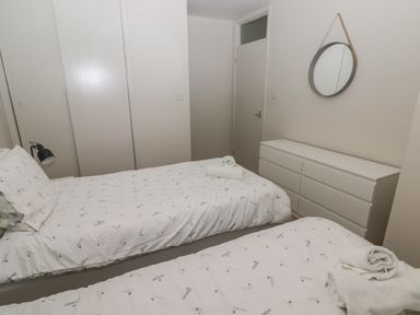 A bedroom with two single beds white dresser round wall mirror and a closed door at 23 Coedrath Park in Saundersfoot