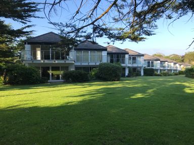 A row of houses with balconies overlooking a large grassy lawn with trees at 23 Coedrath Park in Saundersfoot